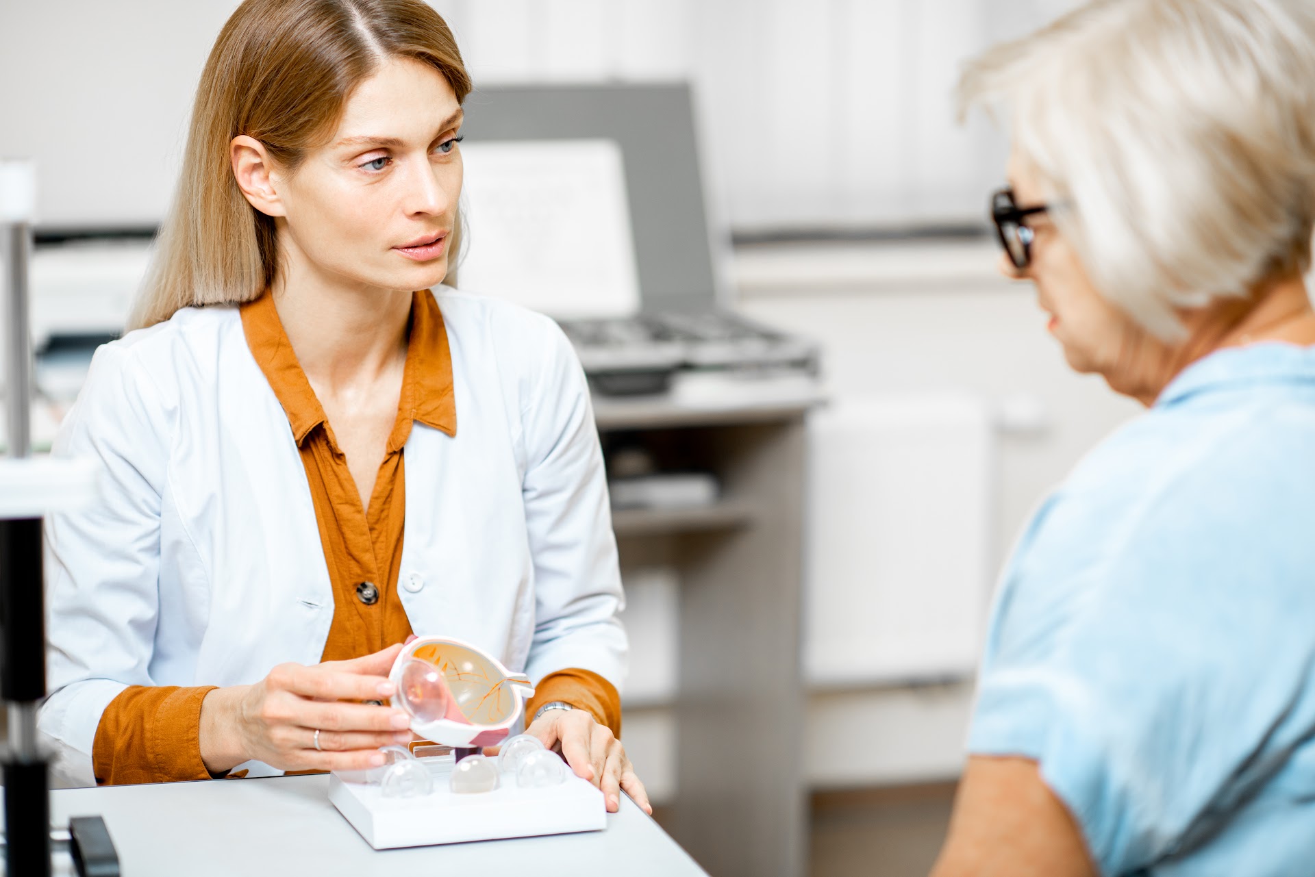 An eye-care professional talking with an older woman at a table